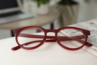 Photo of Glasses and newspaper on armrest indoors, closeup