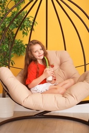 Little girl with glass of delicious milk shake in pendant chair indoors