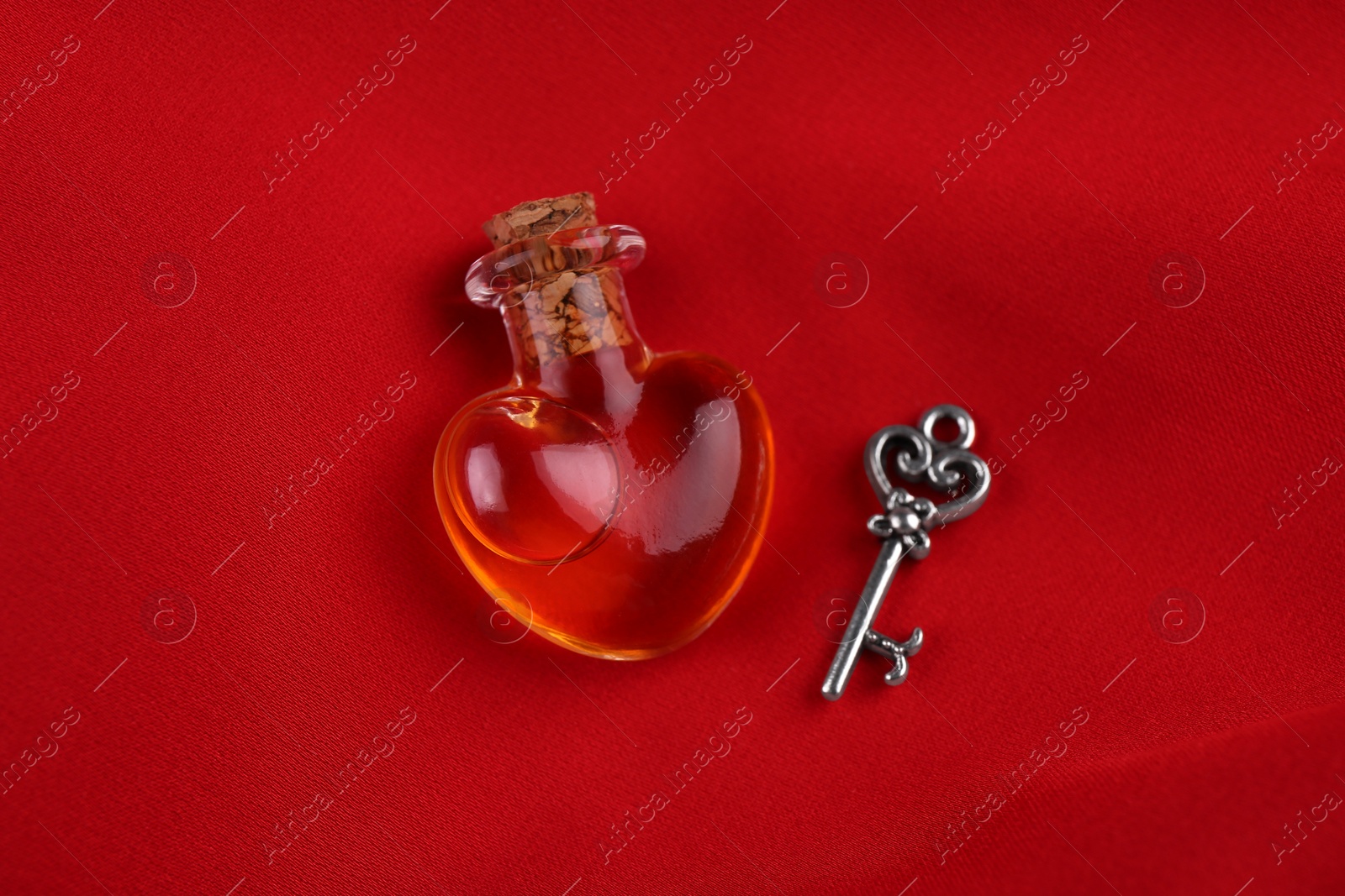 Photo of Heart shaped bottle of love potion with small key on red fabric, above view
