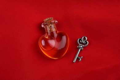 Photo of Heart shaped bottle of love potion with small key on red fabric, above view