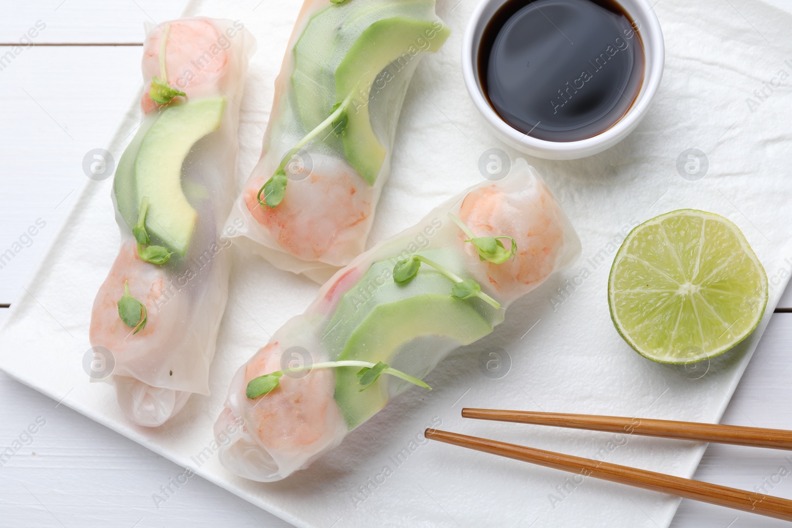 Photo of Delicious spring rolls, lime, soy sauce and chopsticks on white wooden table, top view