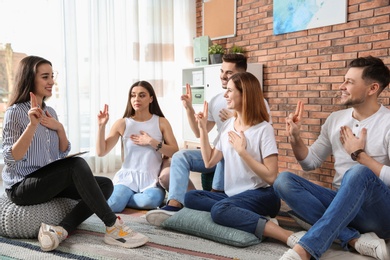 Group of young people learning sign language with teacher indoors