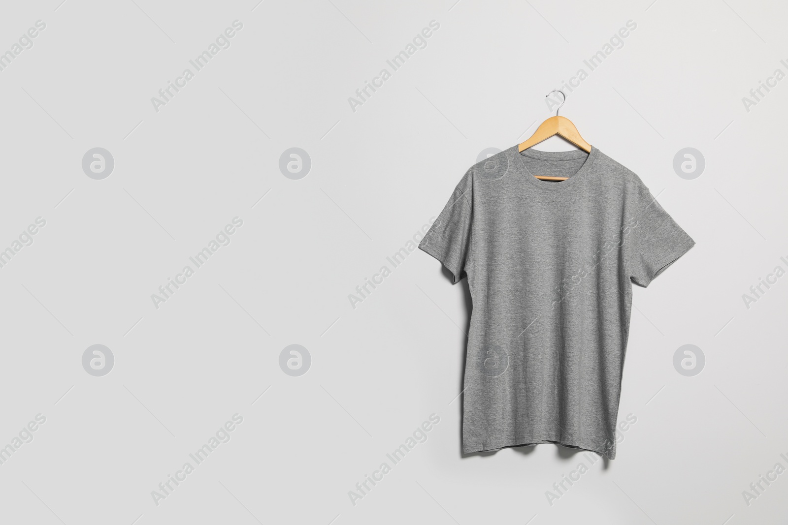Photo of Hanger with grey t-shirt on light wall. Mockup for design