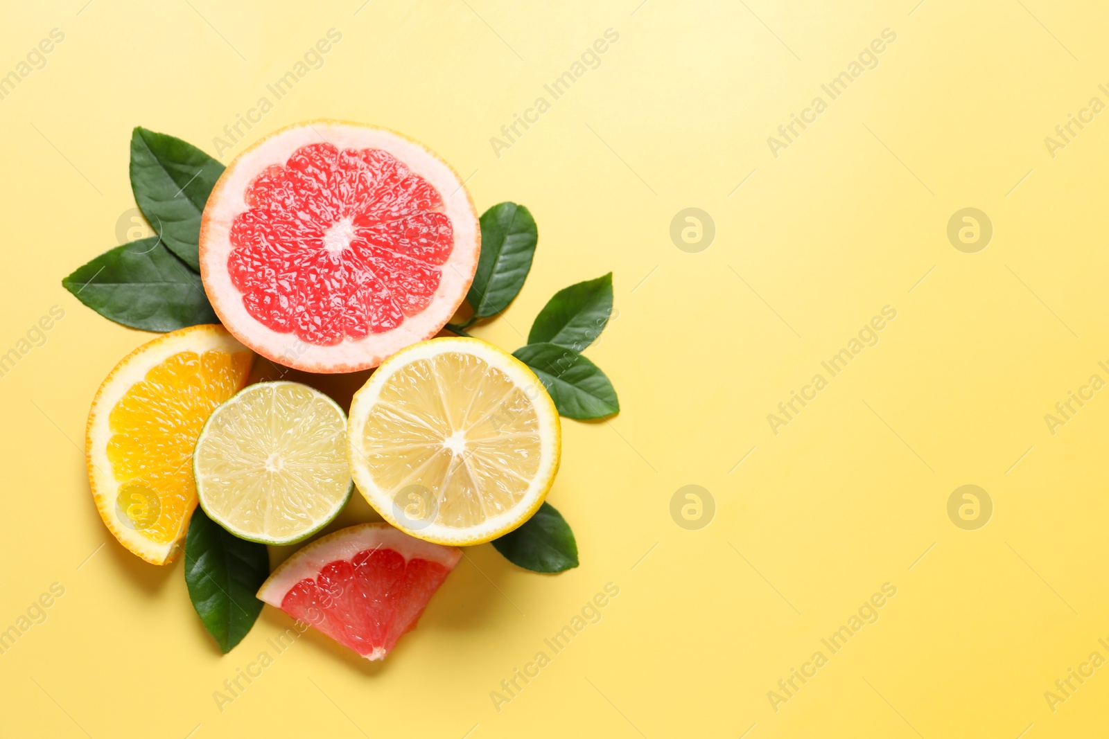 Photo of Different cut citrus fruits and leaves on yellow table, flat lay. Space for text