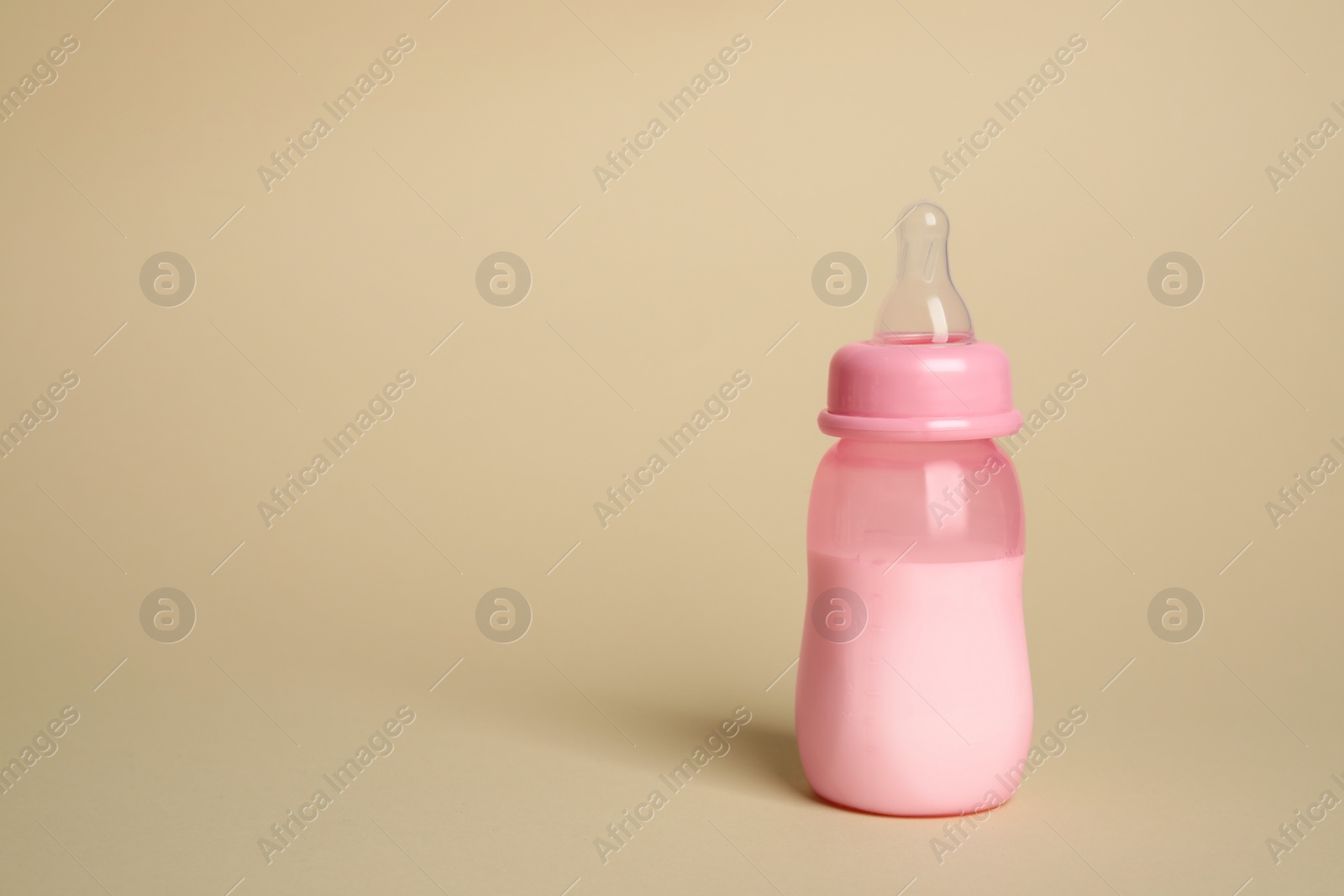 Photo of Feeding bottle with infant formula on beige background. Space for text