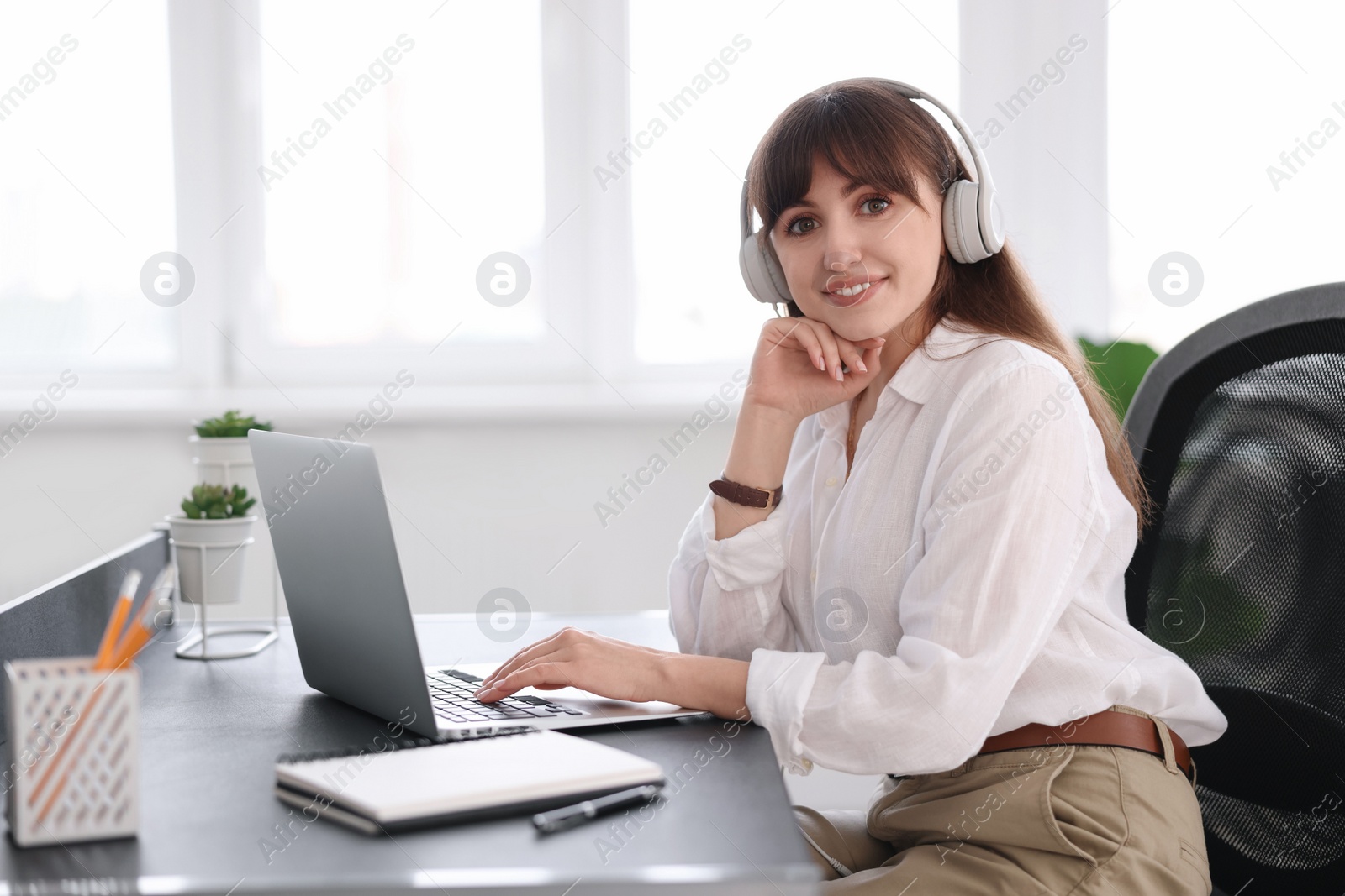 Photo of Woman in headphones watching webinar at table in office