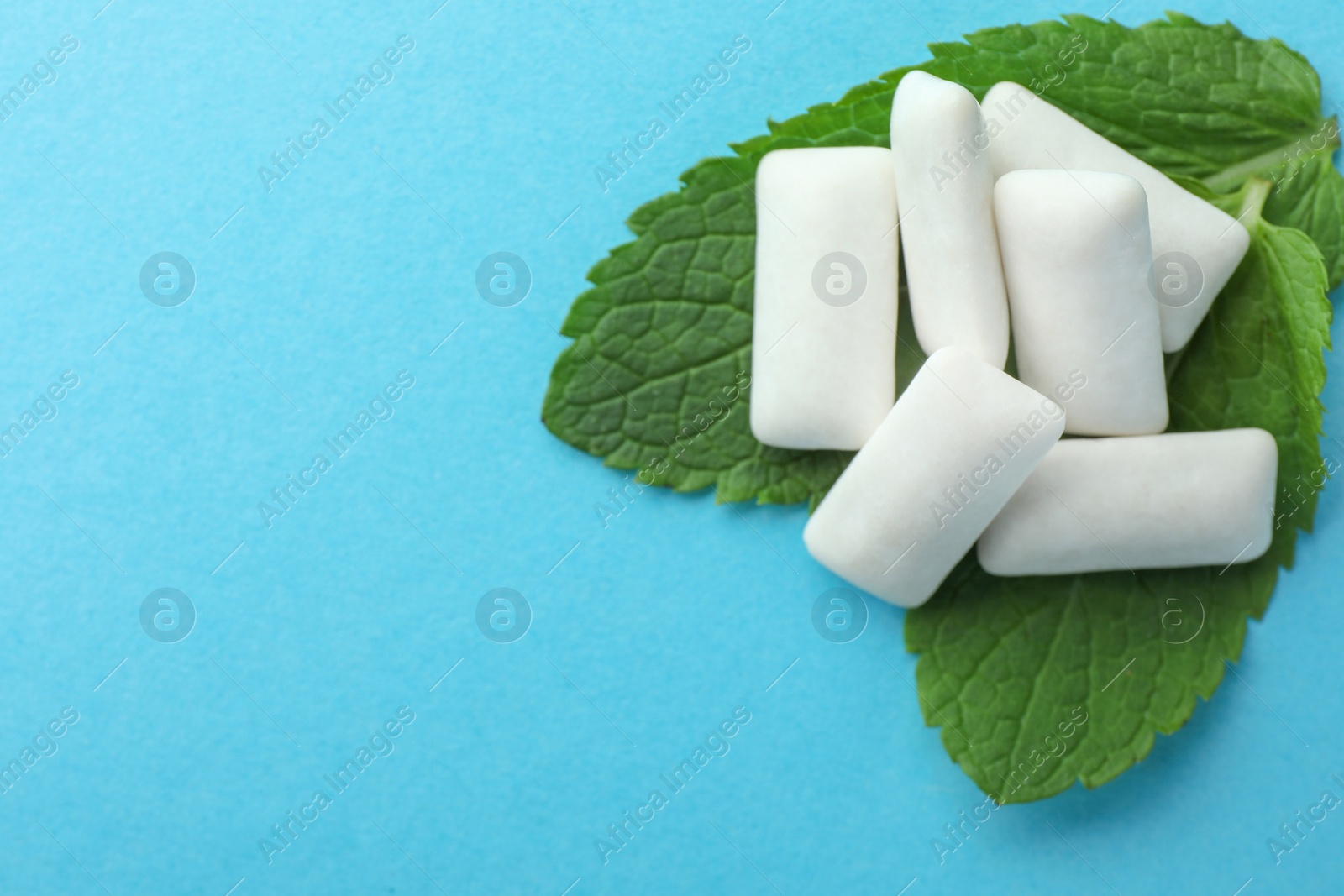 Photo of Tasty white chewing gums and mint leaves on light green background, above view. Space for text