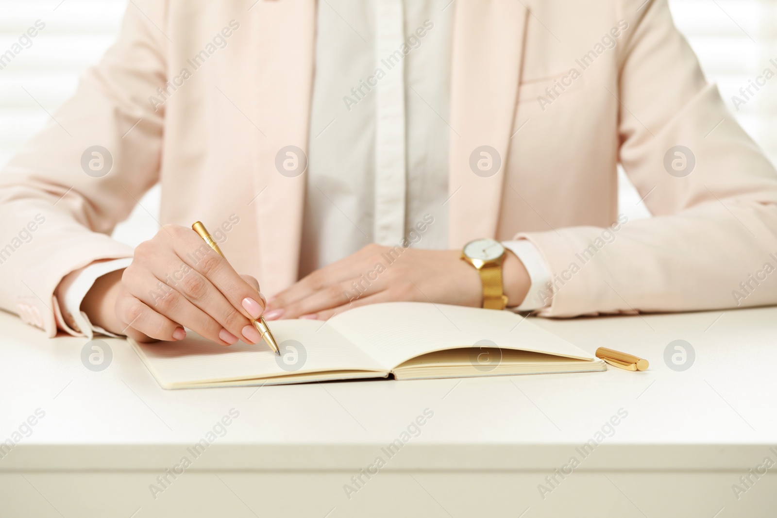 Photo of Woman writing in notebook at white table, closeup