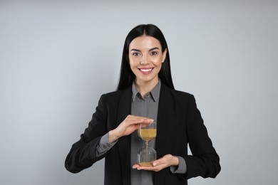 Photo of Businesswoman holding hourglass on light grey background. Time management