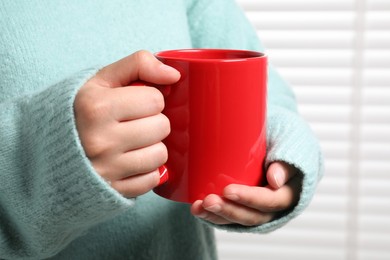 Photo of Woman holding red mug indoors, closeup. Mockup for design