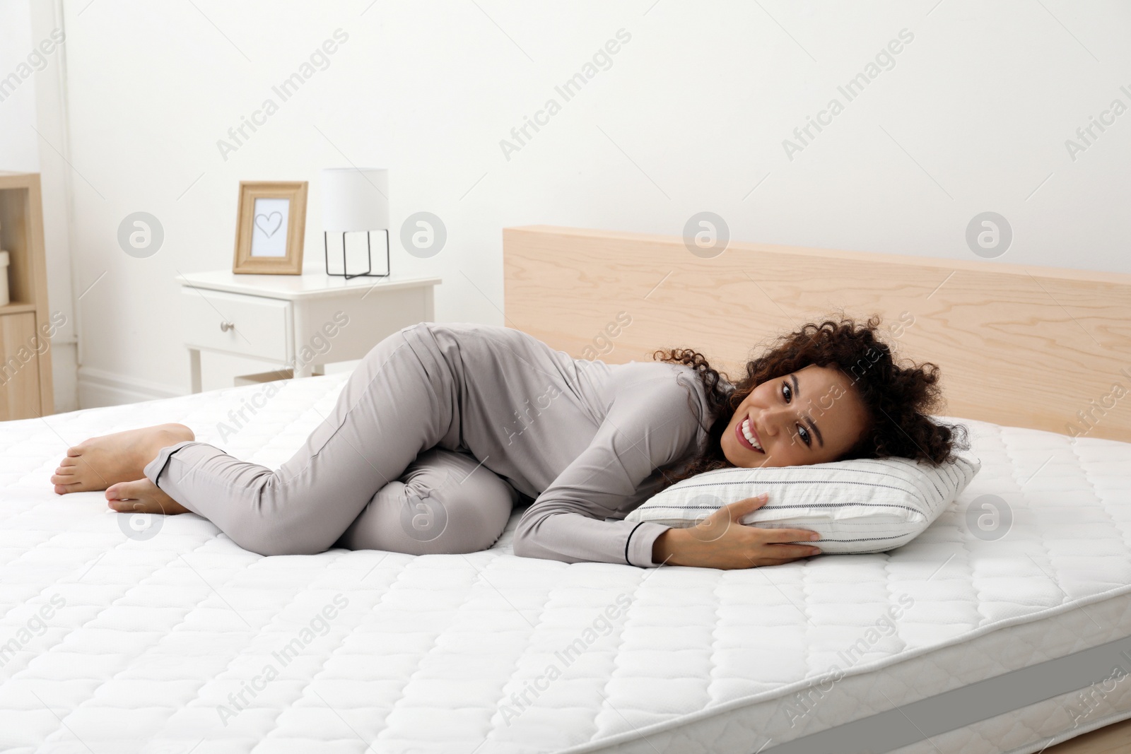 Photo of Happy young African American woman on bed with comfortable mattress and pillow at home