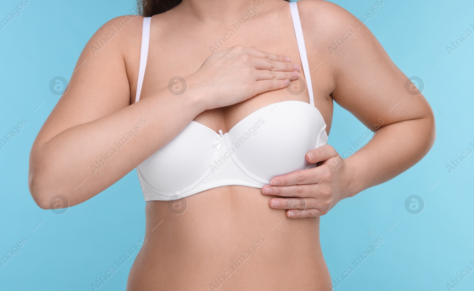 Photo of Mammology. Woman in bra doing breast self-examination on light blue background, closeup