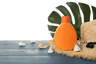 Photo of Sun protection cream, hat, leaf and sea shells on blue wooden table