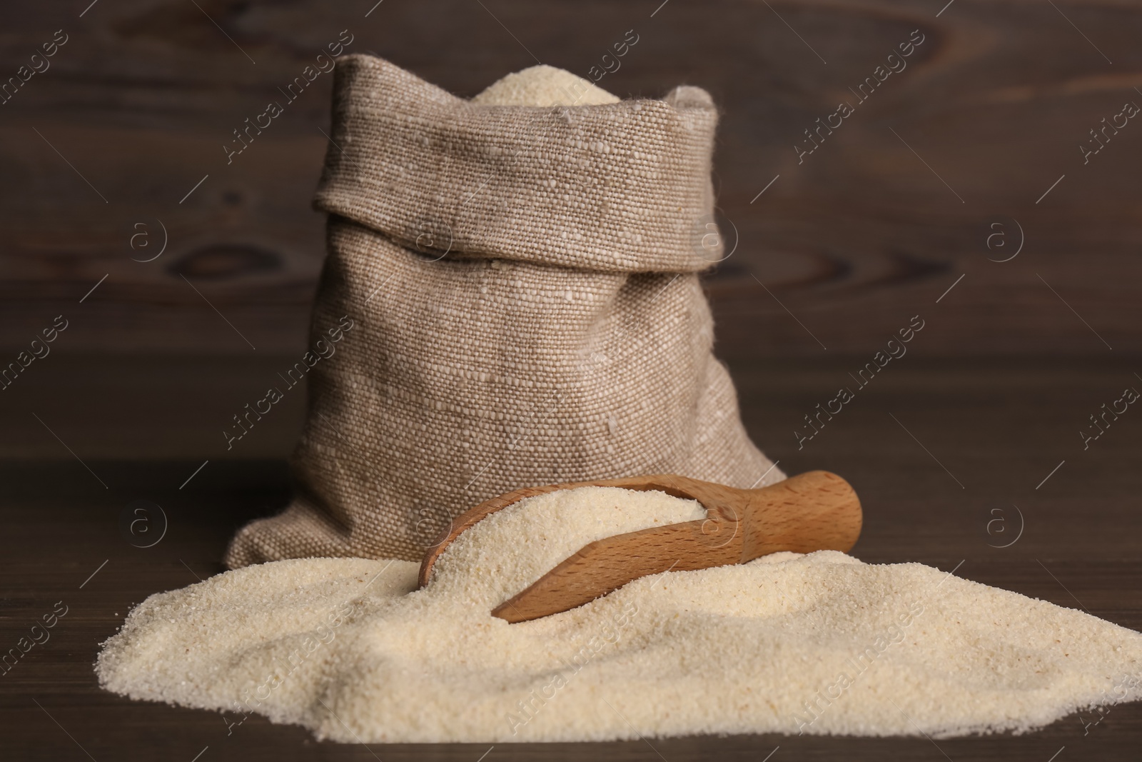 Photo of Bag and scoop with uncooked organic semolina on wooden table