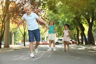 Photo of Little children playing hopscotch drawn with chalk on asphalt outdoors