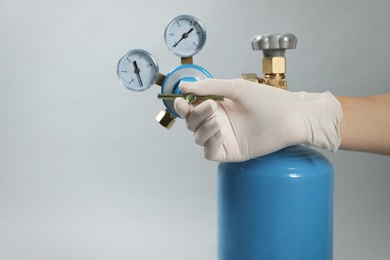 Medical worker checking oxygen tank on light grey background, closeup