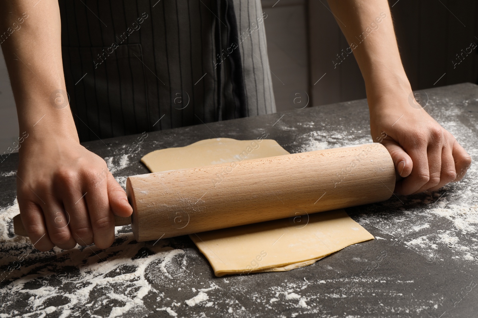 Photo of Woman rolling dough for pasta at grey table, closeup
