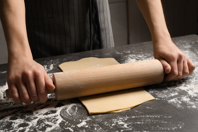 Woman rolling dough for pasta at grey table, closeup