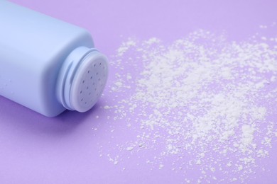 Bottle and scattered dusting powder on violet background, space for text. Baby cosmetic product