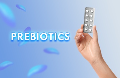 Image of Woman holding pills in blister pack on light blue background, closeup. Prebiotic supplements