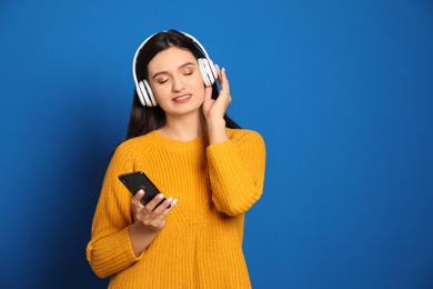 Photo of Young woman listening to audiobook on blue background. Space for text