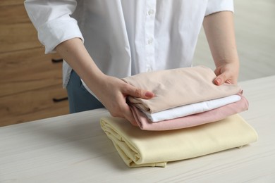 Photo of Woman folding clothes at white wooden table indoors, closeup