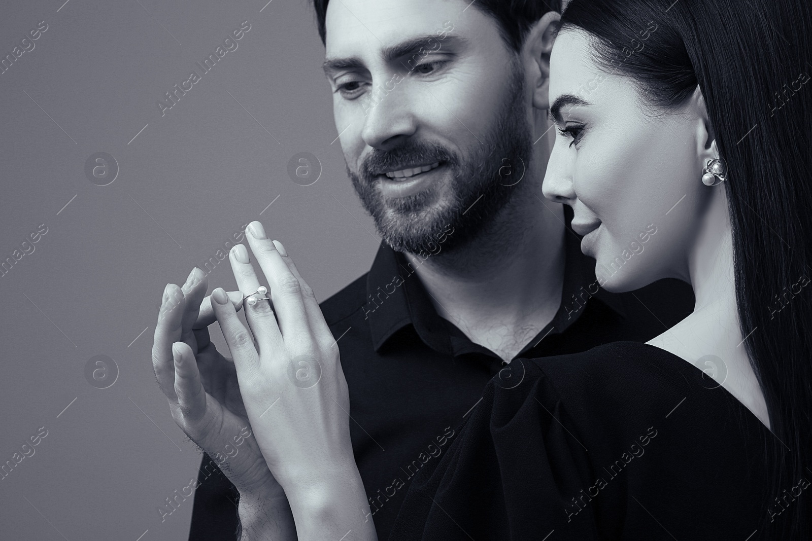 Image of Man putting elegant ring on woman's finger against grey background. Black and white effect