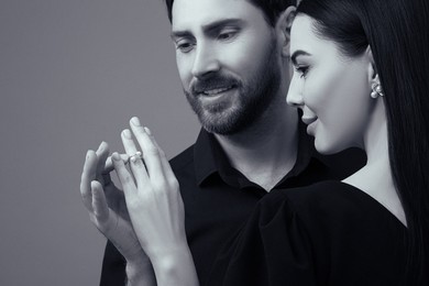 Image of Man putting elegant ring on woman's finger against grey background. Black and white effect