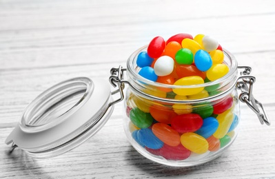 Jar with colorful jelly beans on white wooden background