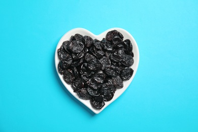 Photo of Heart shaped plate of sweet dried plums on color background, top view. Healthy fruit