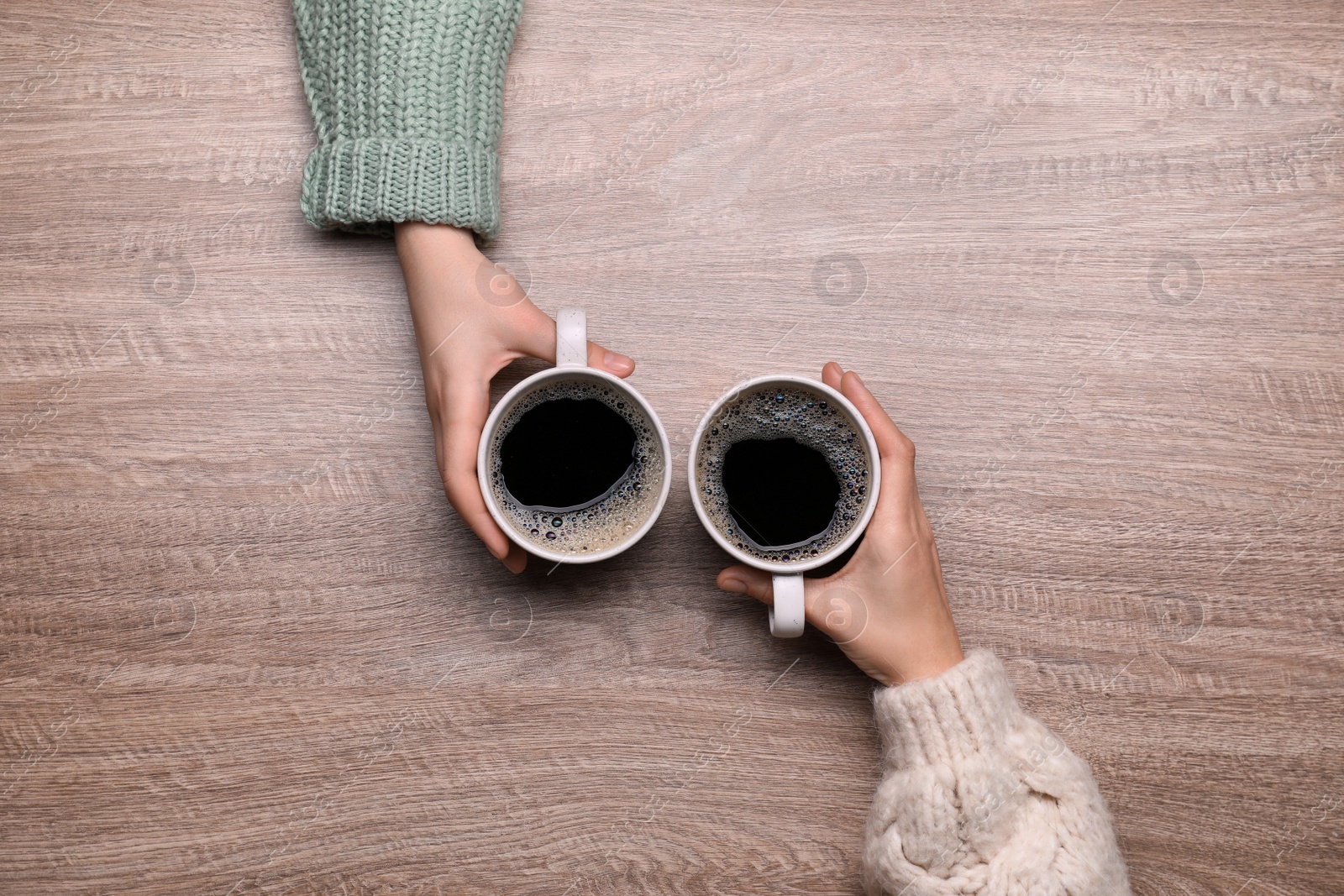 Photo of Women with cups of coffee at wooden table, top view