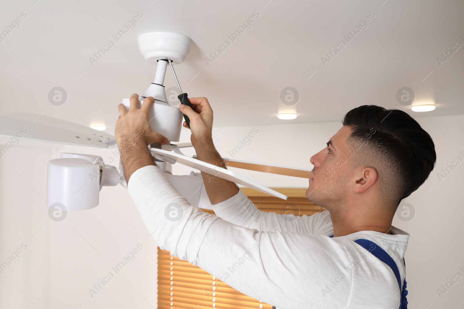 Photo of Electrician with screwdriver repairing ceiling fan indoors