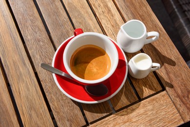 Photo of Cup of aromatic hot coffee, milk and water on wooden table, above view