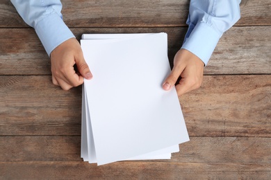 Man holding blank paper sheets for brochure at wooden table, top view. Mock up