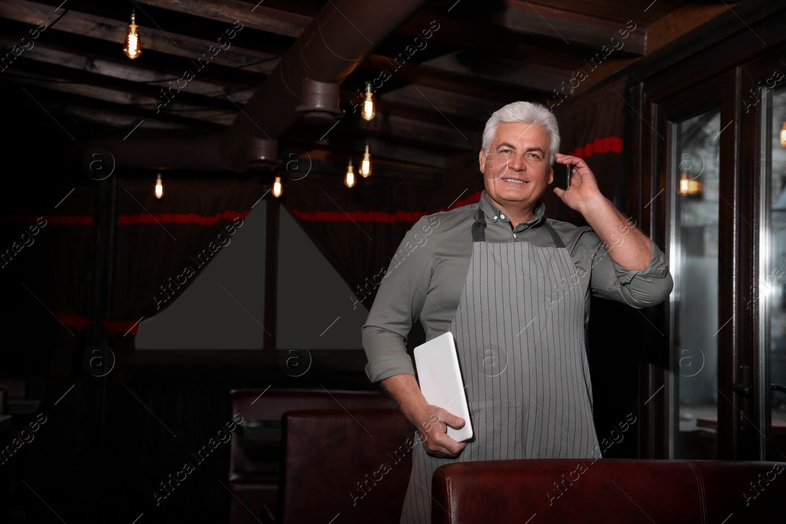 Photo of Senior business owner talking on phone in his restaurant