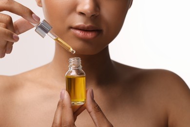 Woman with bottle of serum and dropper on white background, closeup