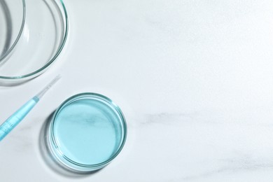 Pipette and petri dishes with liquid on white marble table, flat lay. Space for text