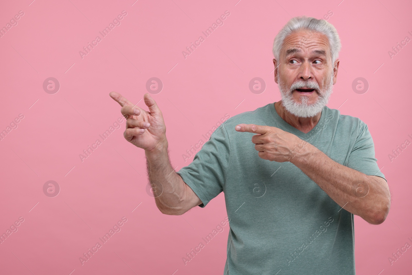 Photo of Special promotion. Senior man pointing at something on pink background. Space for text