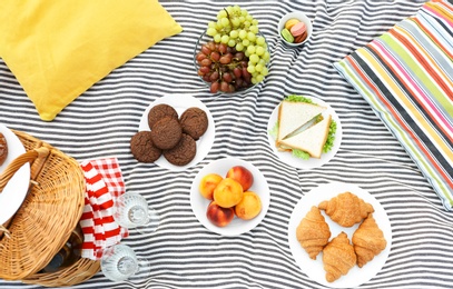 Picnic basket and different snacks on blanket, flat lay