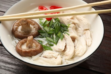 Delicious ramen with meat in bowl and chopsticks on wooden table, closeup. Noodle soup