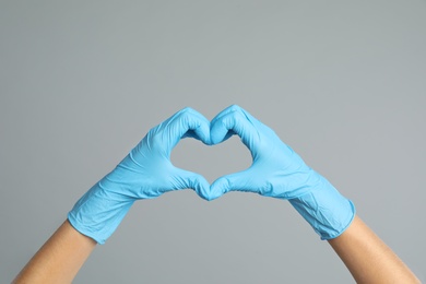 Photo of Doctor in medical gloves showing heart with hands on grey background, closeup