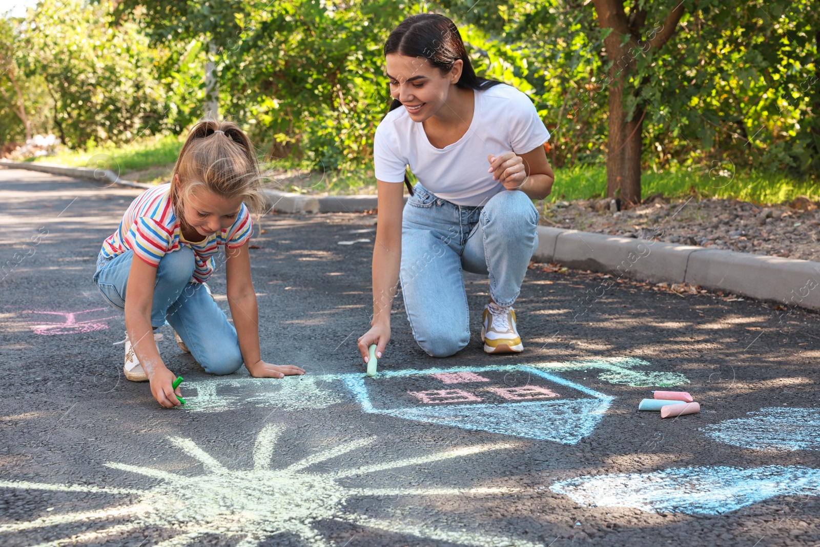 Photo of Cute little child and her mother drawing with colorful chalks on asphalt