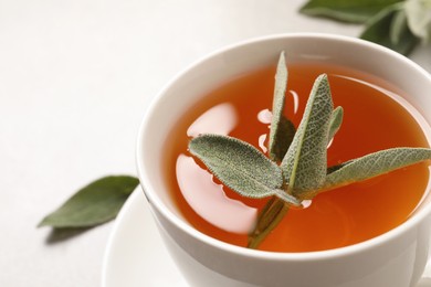 Photo of Cup of aromatic sage tea with fresh leaves on table, closeup