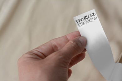 Photo of Woman holding white clothing label on beige garment, closeup
