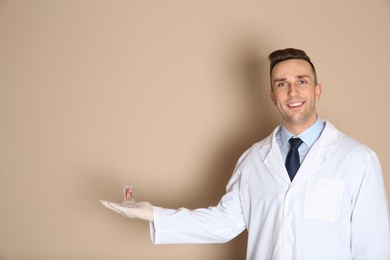 Photo of Male dentist holding tooth model on color background. Space for text