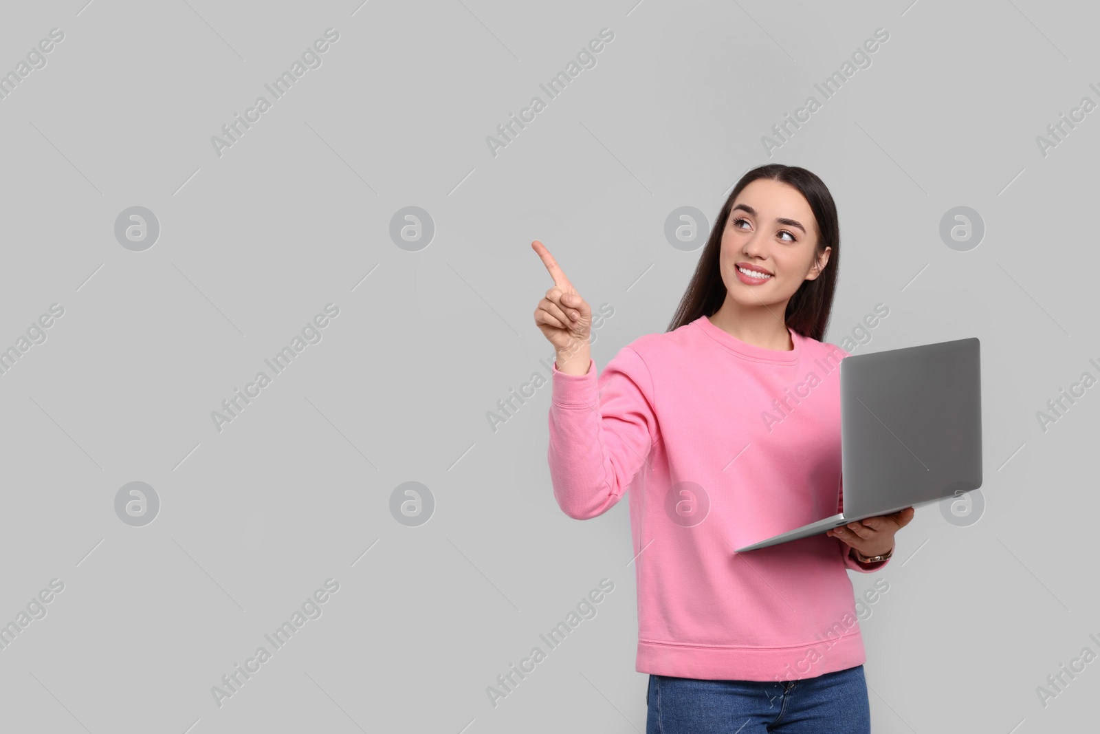 Photo of Smiling young woman with laptop on grey background, space for text