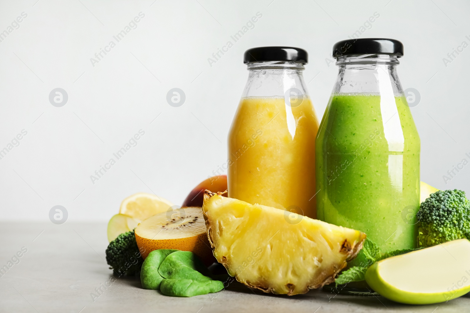 Photo of Bottles of delicious juices and fresh fruits on grey table. Space for text