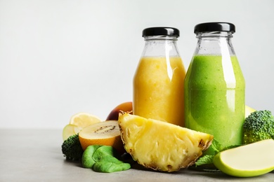 Bottles of delicious juices and fresh fruits on grey table. Space for text