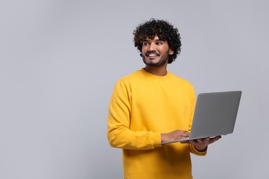 Smiling man with laptop on light grey background, space for text