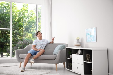 Photo of Young man with air conditioner remote at home